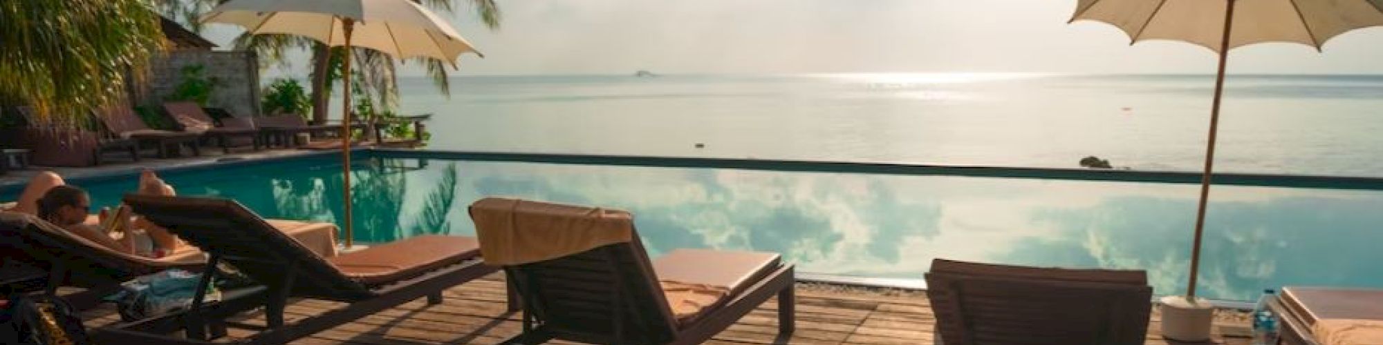 A serene beachside setting with lounge chairs, umbrellas, and an infinity pool facing the ocean under a partly cloudy sky, creating a tranquil atmosphere.