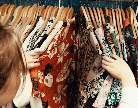 A person browsing through a rack of colorful, patterned clothes on wooden hangers in what appears to be a clothing store.